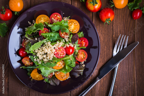 Fresh healthy salad with quinoa, cherry tomatoes and mixed greens (arugula, mesclun, mache) on wood background top view. Food and health. Superfood meal.