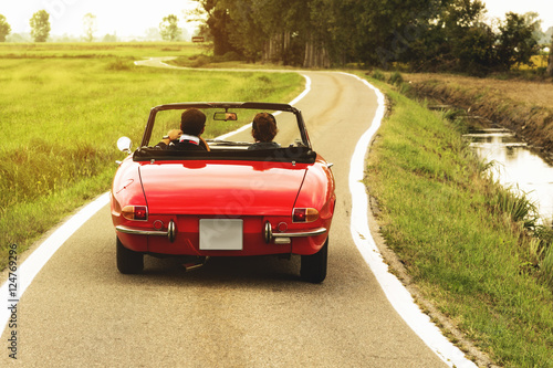 Classic red convertible car traveling in the countryside at sunset