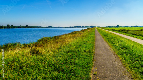 TStraight bicycle path over the dike along the the bird sanctuary of Veluwemeer surrounded by reed and meadows under blue sky near the town of Nijkerk in the Netherlands
