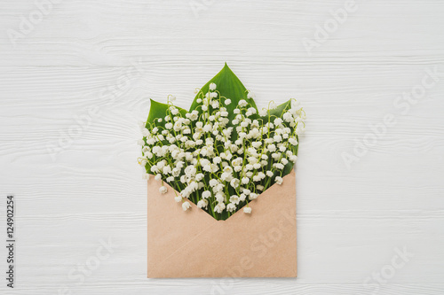 Lily of the valley on white wooden background. Top view of lily of the valley bouquet in craft envelope. Lily of the valley with copy space.