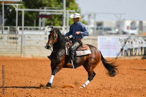 The side view of a rider in cowboy chaps, boots and hat on a horseback performs an exercise during a competition