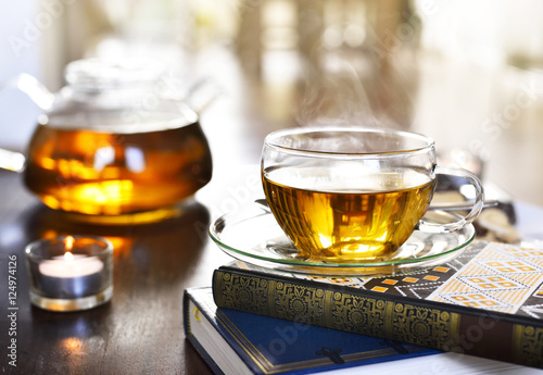 Teatime scene, cup of tea on a book stack with burning candles and selective focus.