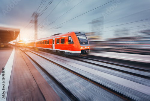Beautiful railway station with modern high speed red commuter train with motion blur effect at colorful sunset. Railroad with sunlight. Vintage toning. Travel. Train