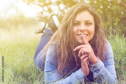 Smiling long haired teenage girl is lying outdoors in sun light. Girl is looking at the camera. 