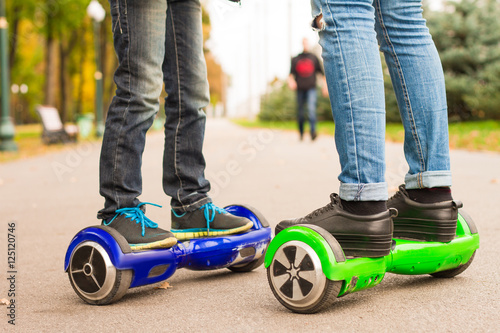 Feet of girl and boy riding electric mini segway outdoors in park