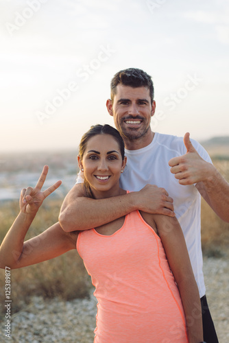 Young couple of successful athletes doing thumbs up gesture after running. Success in sport and healthy lifestyle concept.