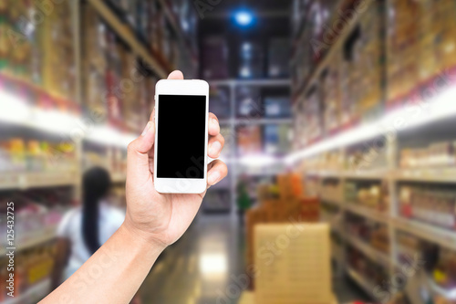 Male hand holding mobile smart phone on Supermarket blur backgro