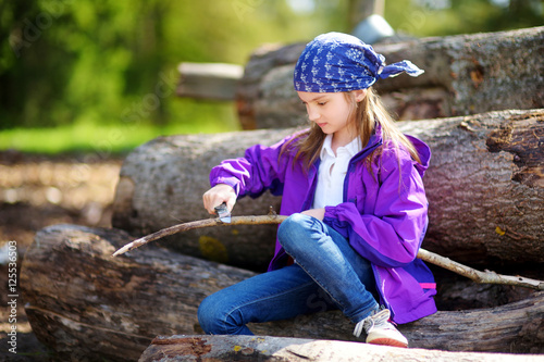 Cute little girl using a pocket knife to whittle a stick for a forest hike