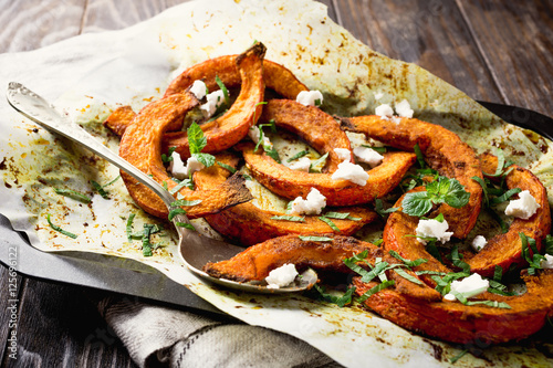 Roasted, baked pumpkin with addition aromatic herbs, goat cheese and mint. Healthy food concept with copy space.