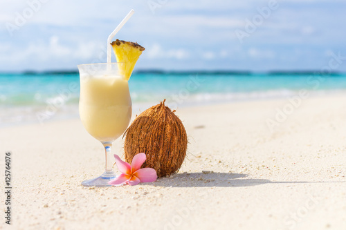 Pina Colada cocktail on the beach with coconut and exotic flower