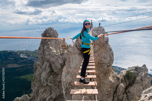 The girl goes on suspension bridge over the precipice