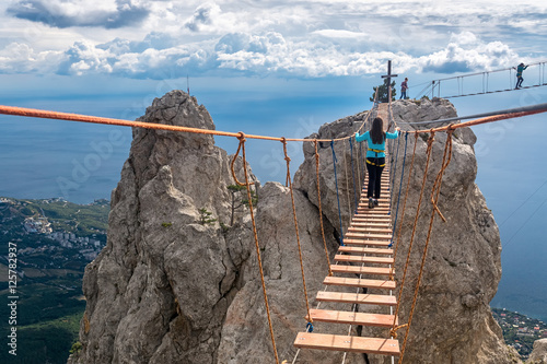 The girl goes on suspension bridge over the precipice