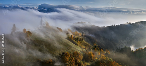 In the morning mist, St. Primoz church near Jamnik at dusk with alps in background, Slovenia