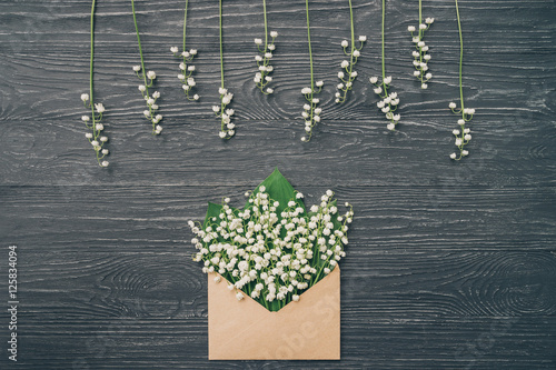 Lily of the valley on gray wooden background. Top view of lily of the valley bouquet in craft envelope. Lily of the valley with copy space.