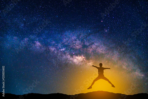 Landscape with Milky way galaxy. Night sky with stars and silhouette jumping man on the mountain.