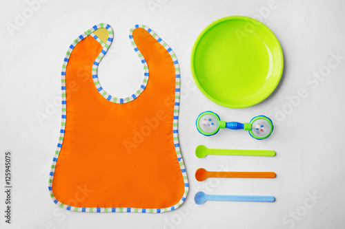 Bright baby tableware and bib on white background