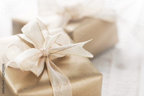 Golden gift boxes with beautiful ribbon and bow on a bright shiny background, holiday concept, horizontal with copy space