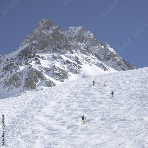 Unidentified skiers are on the snowy slope into Grand Tourmalet ski resort against the mountain range in the French Pyrenees