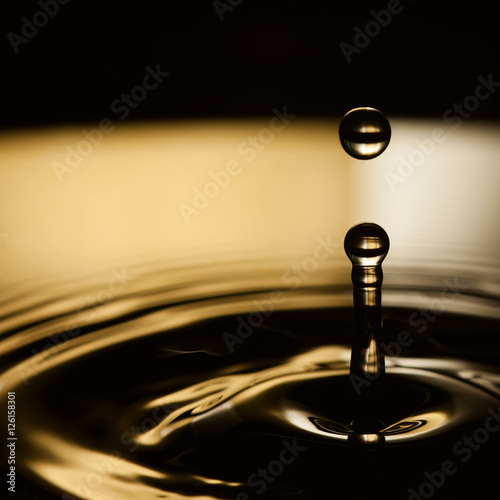 Water splashing. Dropping water bubble. Rings waves in dark bronze and black liquid splash. macro view, soft focus