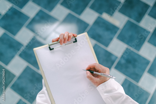 Female doctor in white uniform writing on clipboard paper