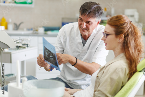 Senior male dentist in dental office talking with female patient and preparing for treatment.Examining x-ray image.