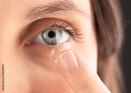 Close up view of young woman putting contact lens in her eye