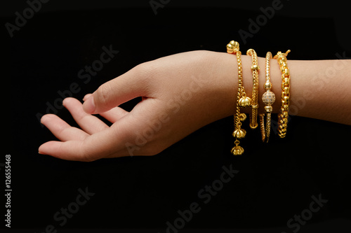 woman's hand with many different golden bracelets on black backg
