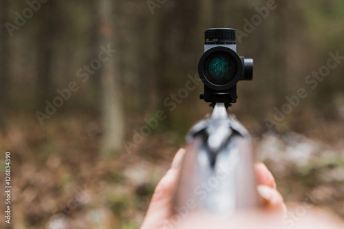 Hunting rifle sight, close-up. Optical sight. A red dot. A man holding a gun.