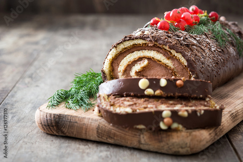 Chocolate yule log christmas cake with red currant on wooden background 