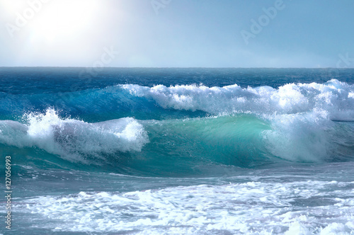 Beautiful big waves of the ocean or the sea in the summer bright blue, azure and turquoise colors in the early morning in sun light on a pure blue sky. Beautiful combs white sea foam.