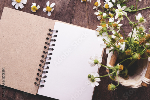 Blank notebook with white flower and bas ket of flower on vintage wooden table View from above with copy space