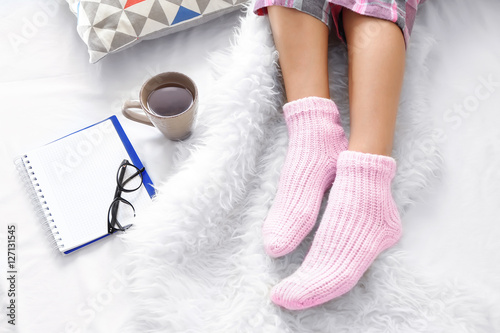 Female feet in socks, cup of tea and notepad on bed