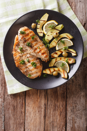 Grilled chicken breast with avocado, lemon and olive close-up. Vertical top view