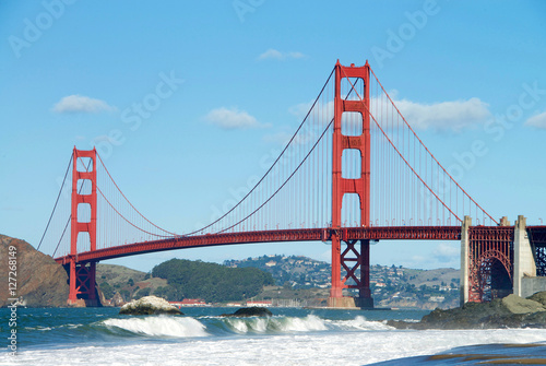 Golden Gate Bridge, viewed from Baker Beach during King Tide phenomenon at high tide with waves crashing over the beach in foreground, blue cloudy sky and Marin hills in background