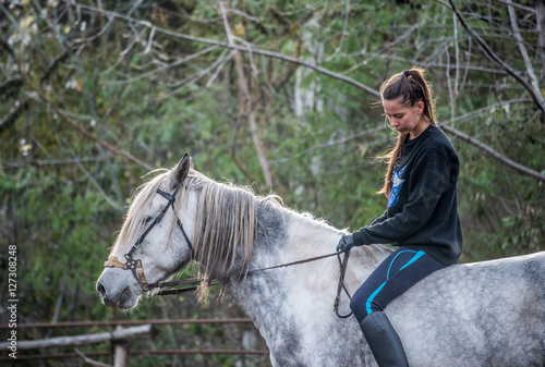 Young beautiful brunette girl rides a horse on a warm and sunny autumn day. Portrait of a pretty young woman on the horse, wearing tall boots and gloves.