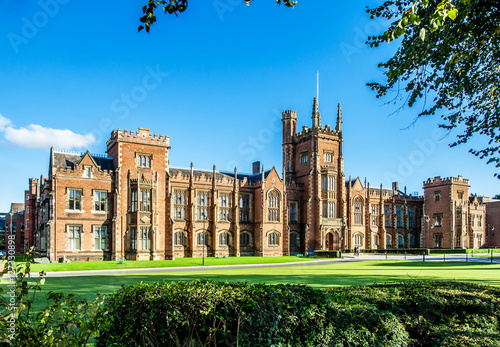 The Queen's University of Belfast with a grass lawn, tree branches and a hedge in sunset light