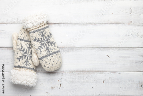 White knitted mittens with winter snowflakes pattern on white wooden background