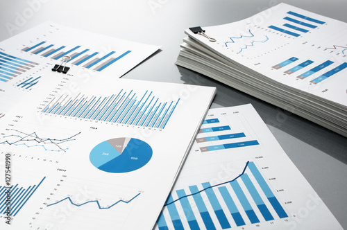 Prepareing report. Blue graphs and charts. Business reports and pile of documents on gray reflection background. 