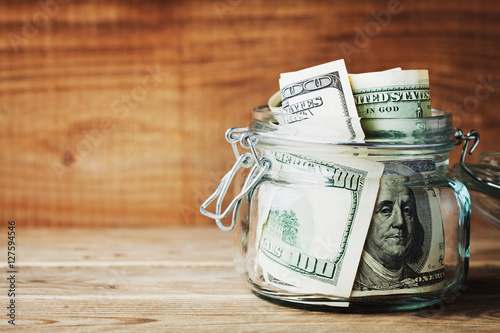 Dollar bills in glass jar on wooden background. Saving money concept.