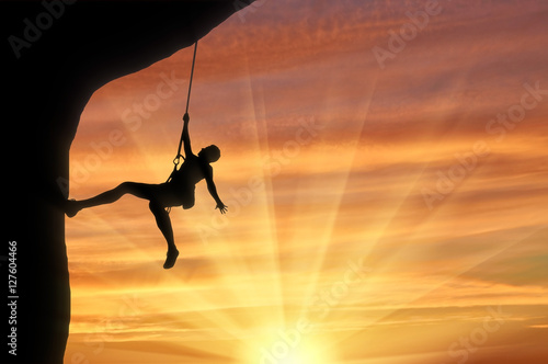 Mountaineer climbing on rock on sunset background