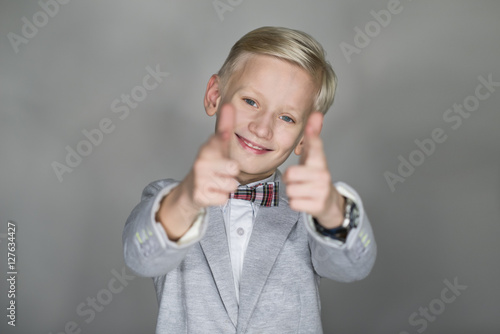 Elegancko ubrany i uśmiechnięty chłopiec z kciukami w górę