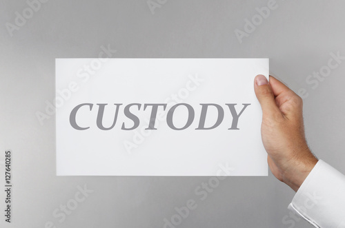 Male hand holding paper with word CUSTODY on gray background
