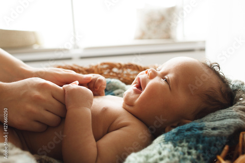 Baby smiling at mother, close-up. Adorable newborn child looking up at mother and holding her hands. Love, innocence, cuteness concept