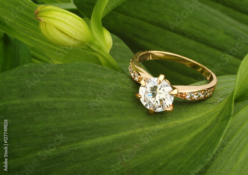 Jewellry ring with big diamond on green leafs background, copysp