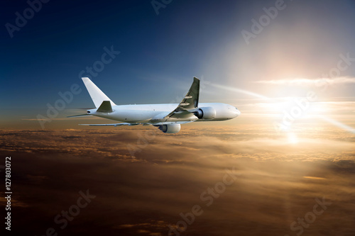 White Cargo plane in the sunset sky. Aircraft flying above the colorful clouds on a background of the bright sun.