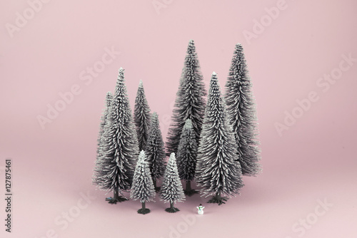 Bodegón mininalista de bosque en invierno con un diminuto muñeco de nieve. Fondo rosa.