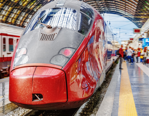 Trenitalia Frecciarossa (red arrow) on platform of Milan Central Station. This high speed train can reach 300 km/h and operate Turin-Milan-Bologna-Florence-Rome-Naples route. Passanger staying nearby.