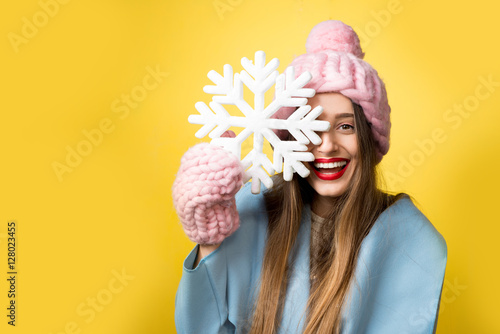 Happy woman in colorful winter clothes holding a beautiful snowflake standing on the yellow background. Happy winter concept