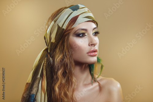 Beauty portrait of a beautiful girl in a scarf with a bright golden Arabic makeup on a beige background.