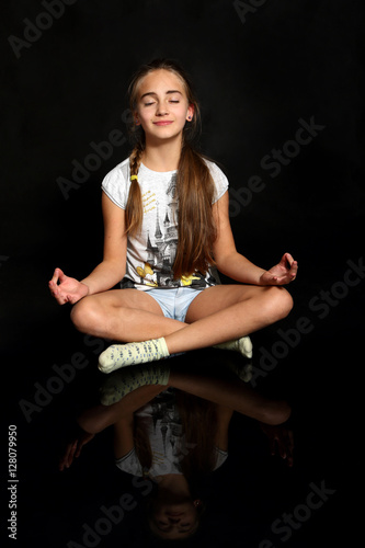 Śliczna dziewczynka medytuje, ćwiczy jogę, na czarnym tle.